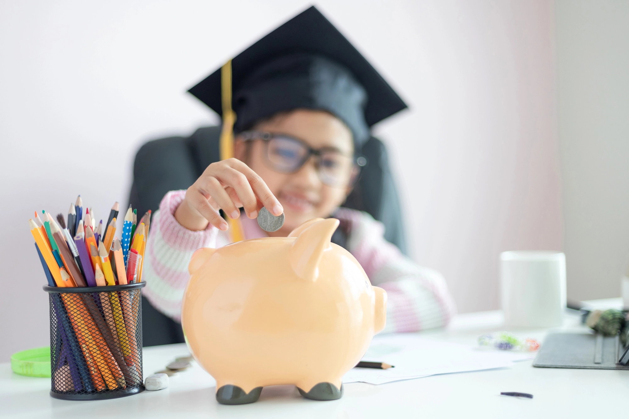 Aides apprentissage 2026 : une jeune fille avec une toque d'étudiant met une pièce dans une tirelire